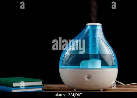 Winternacht, Kälte, Grippe-Konzepte mit einem Ultraschall-Luftbefeuchter erzeugen kühlen Nebel Wasserdampf. Stapel von Büchern sind auch auf hölzernen Tischplatte gesehen. Stockfoto
