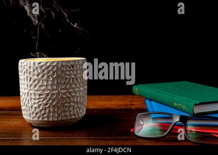 Ein dunkles Bild mit Bücherstapel, Lesebrillen und Steinkerzenhalter auf einem Holzschreibtisch. Aus dem Kerzenhalter kommt Kerzenlicht und Rauch. Vi Stockfoto