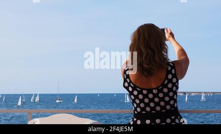 Die Frau fotografiert per Telefon den Windsurfwettbewerb auf dem blauen Meer in Sewastopol, Krim. Stockfoto