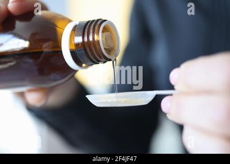 Der Mensch gießt Zuckersirup aus der Flasche in den Löffel Stockfoto