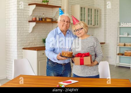 Liebevoller älterer Mann gratulierte seiner Frau zum Jahrestag, indem er ihr ein Geschenk und Kuchen gab. Stockfoto