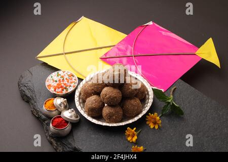 Til Gul ODER Sweet Sesam Laddu mit Drachenmodell, haldi Kumkum und Zuckerkristallen für das Makar Sankranti Festival auf schwarzem Hintergrund. Stockfoto