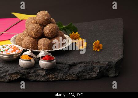 Til Gul ODER Sweet Sesam Laddu mit Drachenmodell, haldi Kumkum und Zuckerkristallen für das Makar Sankranti Festival auf schwarzem Hintergrund. Stockfoto