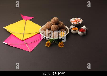 Til Gul ODER Sweet Sesam Laddu mit Drachenmodell, haldi Kumkum und Zuckerkristallen für das Makar Sankranti Festival auf schwarzem Hintergrund. Stockfoto