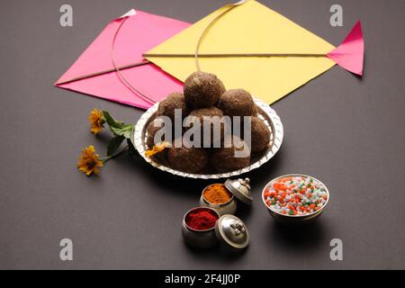 Til Gul ODER Sweet Sesam Laddu mit Drachenmodell, haldi Kumkum und Zuckerkristallen für das Makar Sankranti Festival auf schwarzem Hintergrund. Stockfoto