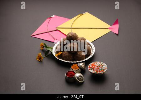 Til Gul ODER Sweet Sesam Laddu mit Drachenmodell, haldi Kumkum und Zuckerkristallen für das Makar Sankranti Festival auf schwarzem Hintergrund. Stockfoto