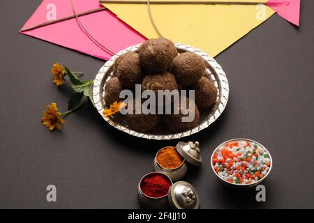 Til Gul ODER Sweet Sesam Laddu mit Drachenmodell, haldi Kumkum und Zuckerkristallen für das Makar Sankranti Festival auf schwarzem Hintergrund. Stockfoto
