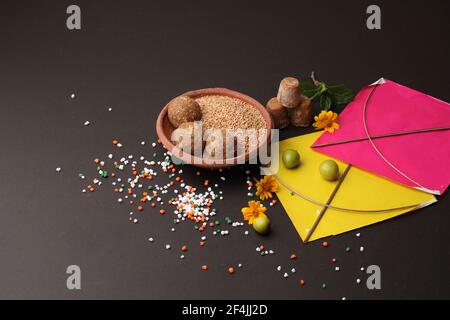 Til Gul ODER Sweet Sesam Laddu mit Drachenmodell, haldi Kumkum und Zuckerkristallen für das Makar Sankranti Festival auf schwarzem Hintergrund. Stockfoto