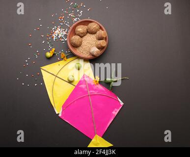Til Gul ODER Sweet Sesam Laddu mit Drachenmodell, haldi Kumkum und Zuckerkristallen für das Makar Sankranti Festival auf schwarzem Hintergrund. Stockfoto