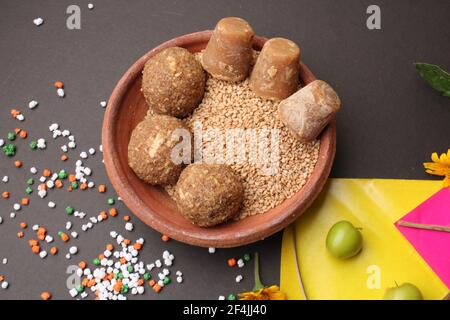 Til Gul ODER Sweet Sesam Laddu mit Drachenmodell, haldi Kumkum und Zuckerkristallen für das Makar Sankranti Festival auf schwarzem Hintergrund. Stockfoto