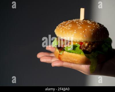 Köstliche frische hausgemachte Burger. Hand hält leckeren hausgemachten Hamburger auf dunklem Hintergrund. Hand zeigt Rindfleisch Burger. Stockfoto