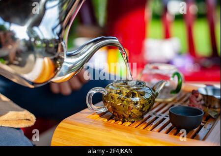 Traditionelle chinesische Teezeremonie. Heißes Wasser, das in eine Glas-Teekanne mit grünen Teeblättern von chinesischem Oolong-Tee hineingießt. Stockfoto