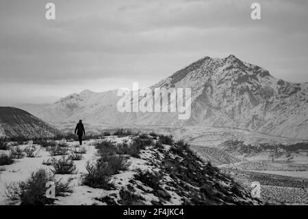 Schwarz-Weiß-Foto einer unbekannten Person, die am Ufer des Azat-Stausees in Armenien entlang wandert, mit dem Berg Yeranos im Hintergrund Stockfoto