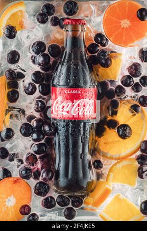 Eine Flasche klassischer Coca Cola und Scheiben von Orange, Blaubeeren, Zitrusscheiben auf dem Hintergrund von Eiswürfeln. Russland, Krasnojarsk, 17. März 2021. Stockfoto