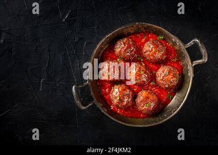 Fleischbällchen in einer gusseisernen Pfanne, aufgenommen von oben auf einem dunklen Hintergrund mit Kopierraum Stockfoto