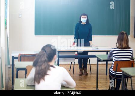 Die Lehrerin und ihre Schüler tragen im Klassenzimmer eine schützende Gesichtsmaske. Soziale Distanz und Klassensicherheit während der Coronavirus-Epidemie Stockfoto