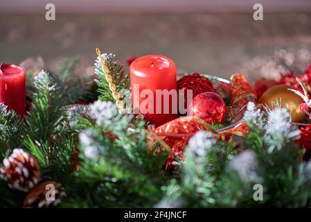 Rote Feiertagskerze zwischen künstlichen Fichtenzweigen und Weihnachtsbaum Dekorationen Stockfoto
