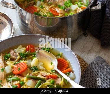 Frische und hausgemachte gekochte Hühnernudelsuppe mit Frühlingsgemüse Serviert auf einem Teller auf einem Tisch mit Topf in Der Hintergrund Stockfoto