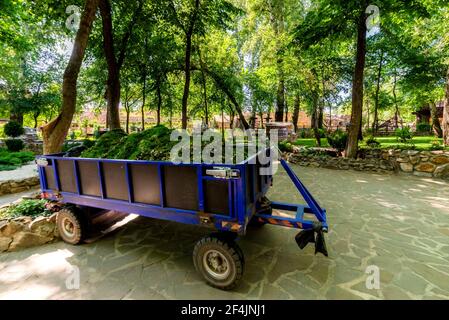 Blauer moderner Anhänger für einen Traktor mit Gras und Boden in einem botanischen Garten. Stockfoto