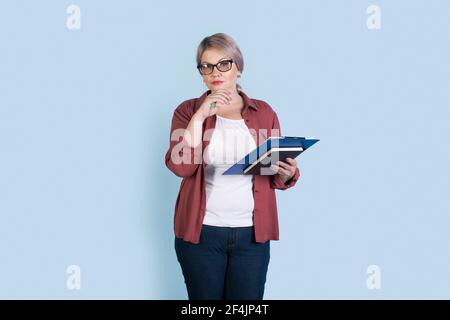 Ältere kaukasische Geschäftsfrau posiert auf einer blauen Studiowand Einige Ordner halten und eine Brille tragen, die auf die Kamera schaut Stockfoto