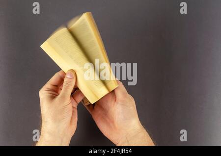 Verschwommene Bewegung der Hand Umdrehen Seite über grauen Hintergrund. Männliche Hände blättern schnell durch ein altes Buch mit vergilbten Seiten. Mann mittleren Alters, kaukasisch. Stockfoto