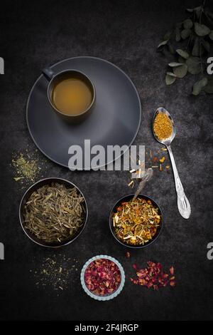 Eine schwarze Tasse Kurkuma Tee mit verschiedenen Tassen Teekräuter auf schwarzer Oberfläche Stockfoto