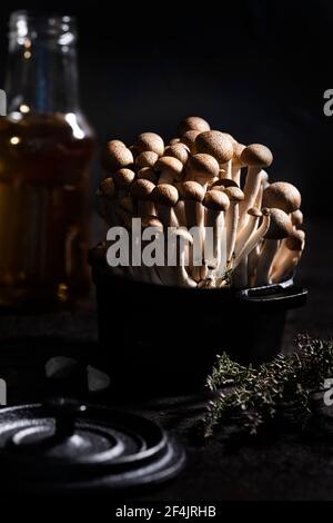 Braune Shimeji Pilzgruppe in einem schwarzen gusseisernen Topf mit Thymian, Knoblauch und Olivenöl verziert Stockfoto