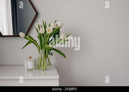 Weiße Tulpen in einer Glasvase auf einer weißen Kommode. Stockfoto