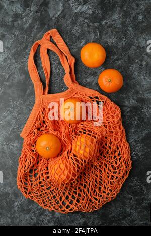 Orange String-Tasche mit frischen Mandarinen auf einem schwarzen rauchigen Hintergrund, umweltfreundliches Einkaufen Stockfoto