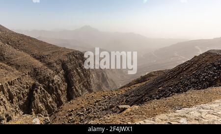 Felsige und karge Hajar Mountains Bergkette mit Dunst am Horizont vom Jebel Jais Aussichtsplattform Park, Vereinigte Arabische Emirate. Stockfoto