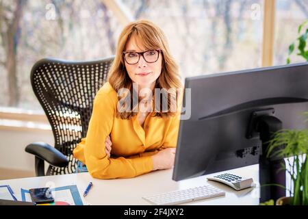 Aufnahme einer lächelnden Geschäftsfrau, die am Schreibtisch hinter ihrem Computer sitzt, während sie arbeitet. Stockfoto