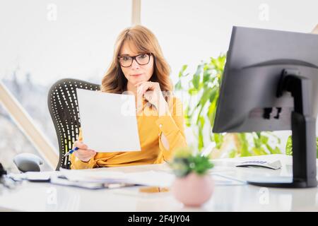 Aufnahme einer selbstbewussten Geschäftsfrau, die das Dokument in der Hand hält, während sie am Schreibtisch sitzt und arbeitet. Stockfoto