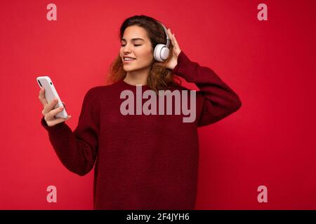 Foto von schönen fröhlich lächelnd junge Frau trägt stilvolle Casual Kleidung isoliert über der Hintergrundwand halten und mit Handy Tragen Stockfoto