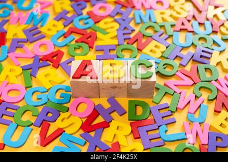 Alphabet auf Holzfliesen und ABC auf einem Würfel vor gelbem Hintergrund. Konzept der Entwicklung der Bildung von Kindern Stockfoto
