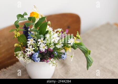 Schöne Frühling Wildblumen in Vintage-Tasse auf rustikalen Holztisch. Blühende bunte Blumen von ajuga, Vergiss-mich-Nots, Narzissen, Pulmonaria, Rabeler Stockfoto
