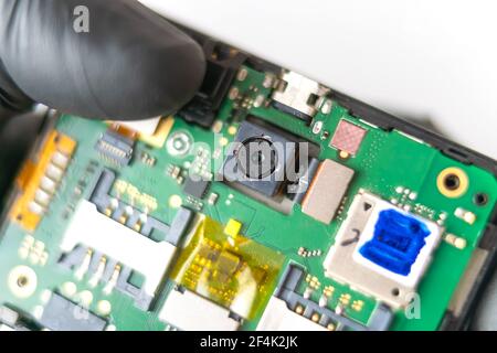Reparieren Sie das Telefon.EIN Techniker oder Meister repariert ein Handy, er installiert und wechselt die Kamera auf der Hauptplatine. Hände, Handschuhe, Makro Stockfoto