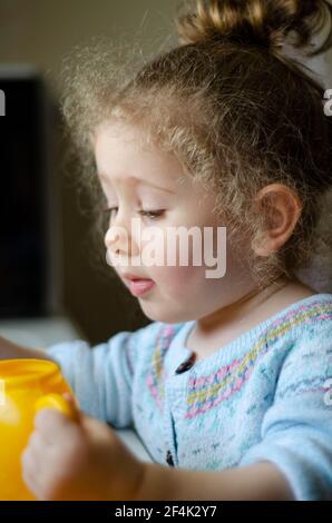 Mollige kleine Mädchen mit flatternden blonden Haaren spielt mit ihrem Spielzeug. Selektive Fokus Wange und Gesicht Stockfoto