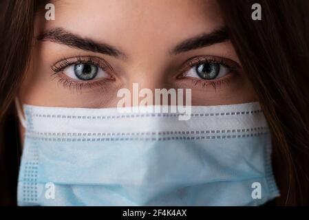 Kopfaufnahme der jungen Frau mit schönen grünen Augen tragen chirurgische Gesichtsmaske. Studioaufnahme. Isolierter Hintergrund. Stockfoto