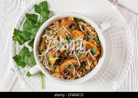 Klassisches cremiges Pilzrisotto mit geriebenem Parmesan und Petersilie in einer weißen Schüssel, Nahaufnahme, flaches Lay, italienische Küche Stockfoto