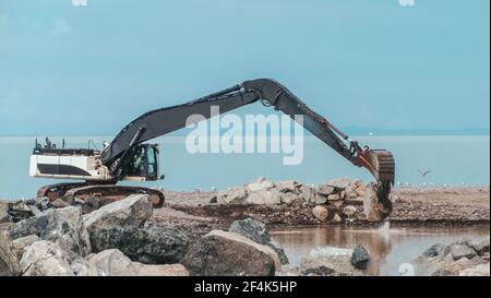 Planierraupen gräbt Sand und Kies im Steinbruch. Schwere Baumaschinen während der Aushubarbeiten auf der Baustelle in der Nähe eines Meeres Stockfoto