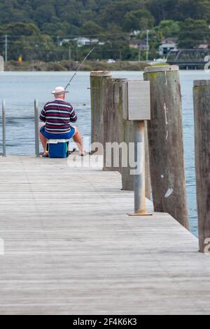 Ein eineinziger älterer Fischer sitzt auf einem Esky Kühler und Fische von einem Kai in Narooma auf dem Neuen Süden Südküste von Wales in Australien Stockfoto