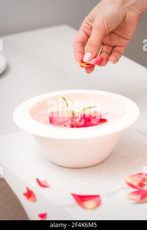 Die weiblichen Hände der Kosmetikerin bereiten das Maniküre-Bad mit Rot und Rosa vor rosenblüten auf dem Tisch im Spa Stockfoto