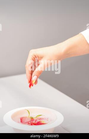 Die weiblichen Hände der Kosmetikerin bereiten das Maniküre-Bad mit Rot und Rosa vor rosenblüten auf dem Tisch im Spa Stockfoto