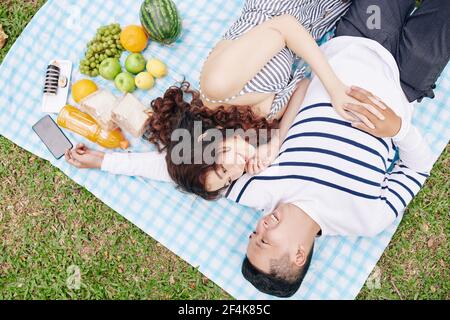 Glücklich umarmt junge vietnamesische Paar auf Decke im Park ruhen und einander nach dem Essen von Suchi und Obst beim Picknick, Blick von oben Stockfoto