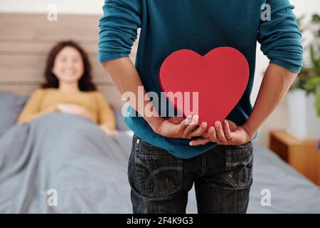 Zugeschnittenes Bild des Mannes versteckt romantische Gegenwart hinter seinem Rücken Als ich im Bett der Freundin stand, die gerade aufwachte Stockfoto