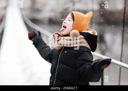 Lustige kleine Mädchen fängt Schneeflocken in einem schönen Winter Park während eines Schneefalls. Niedliches Baby spielt im Schnee. Winteraktivitäten für Kinder Stockfoto