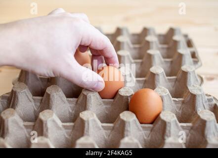 Ein Mann nimmt mit der Hand ein braunes Ei aus einem Pappsack, ein Hühnereier in der Hand zum Kochen, ein Tablett zum Tragen und Aufbewahren zerbrechlicher Eier. Stockfoto