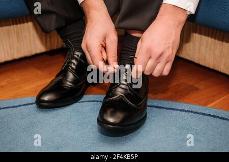 Der Typ bindet die Schnürsenkel auf schwarzen klassischen Schuhen. Der Bräutigam trägt schöne Schuhe und bindet seine Schnürsenkel Stockfoto