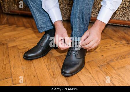 Der Typ bindet die Schnürsenkel auf schwarzen klassischen Schuhen. Der Bräutigam trägt schöne Schuhe und bindet seine Schnürsenkel Stockfoto