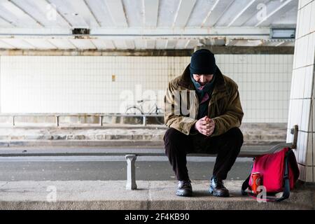 Amsterdam, Niederlande. Homeles Mann sitzt an einem Geländer und tötet seine Zeit, beneith eine Vondelpark Brücke. Stockfoto